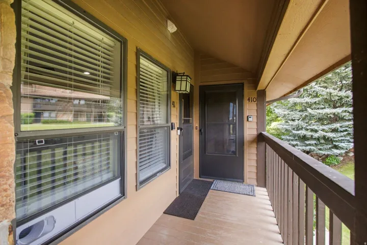 Covered porch entrance featuring a dark brown entry door with a screen, wood-finish siding, and an outdoor wall light fixture