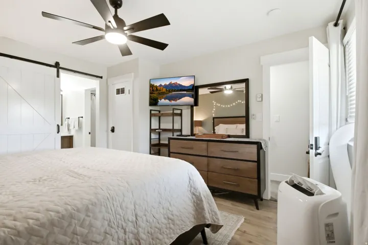 Bedroom featuring wood-finish flooring, a ceiling fan with integrated lighting, a sliding barn door, and a built-in window with horizontal blinds