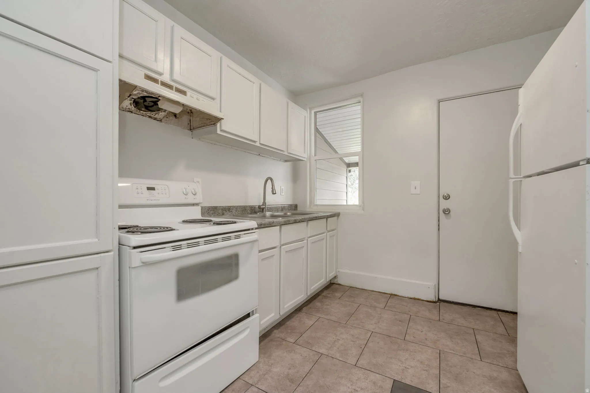 Kitchen featuring white cabinetry, white electric range, white refrigerator, single basin stainless steel sink, and light-toned tile flooring