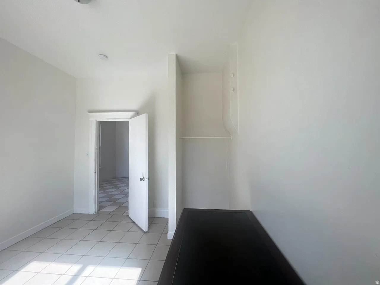 Room featuring light-toned tile flooring, white walls, and a built-in shelf