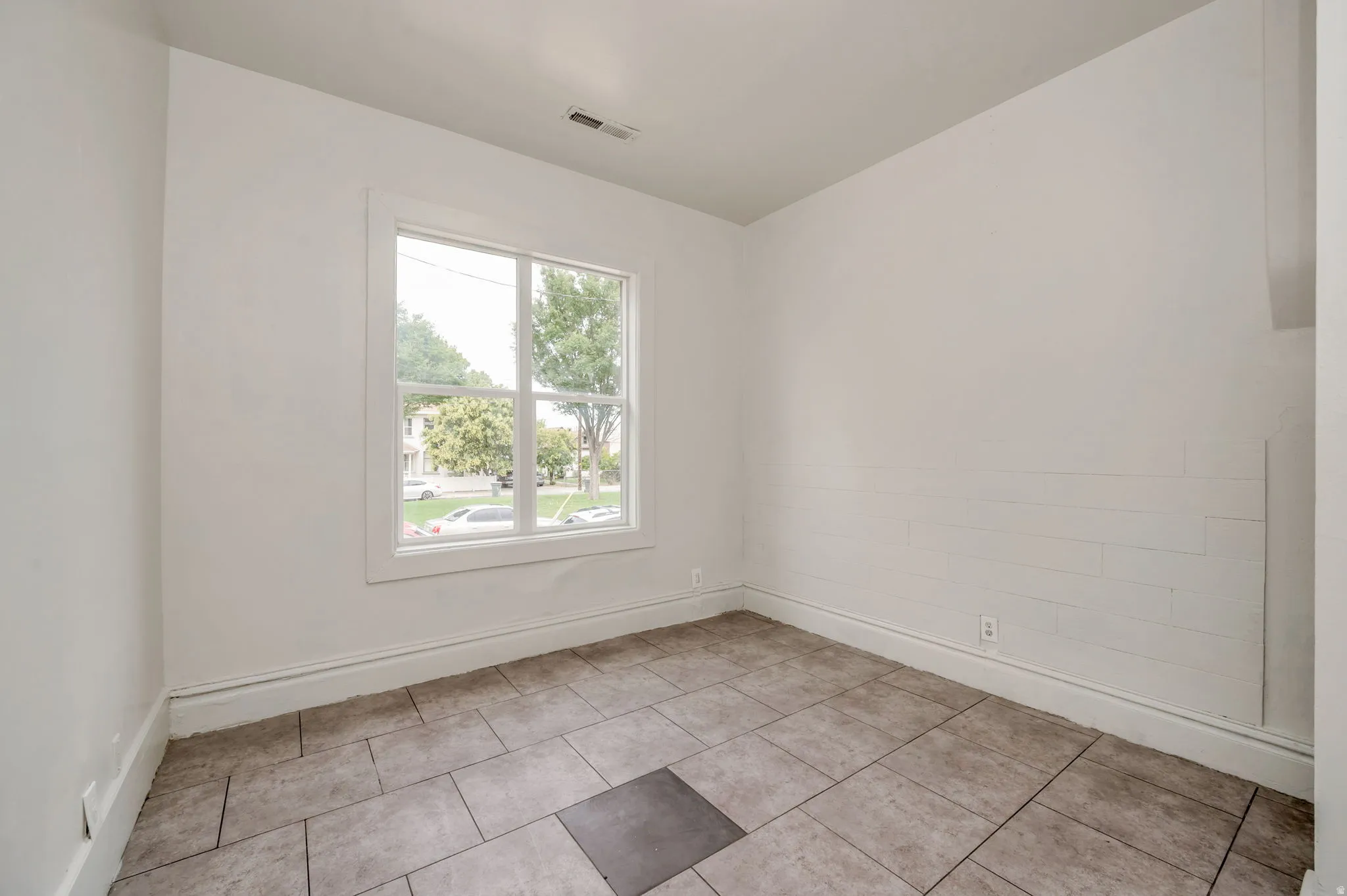 Room with a double-hung window, light-toned walls, and rectangular floor tiles