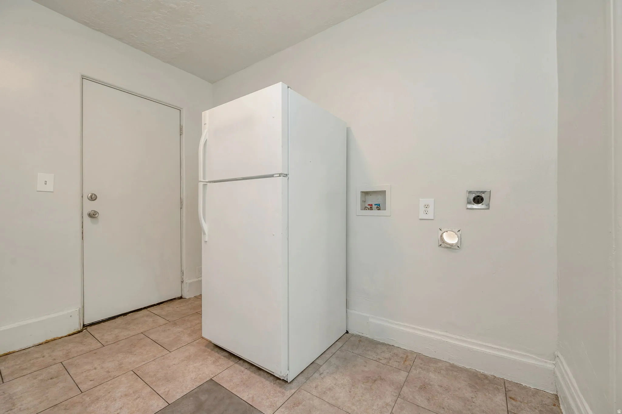 Utility area featuring a top-freezer refrigerator, tile flooring, and light-colored walls