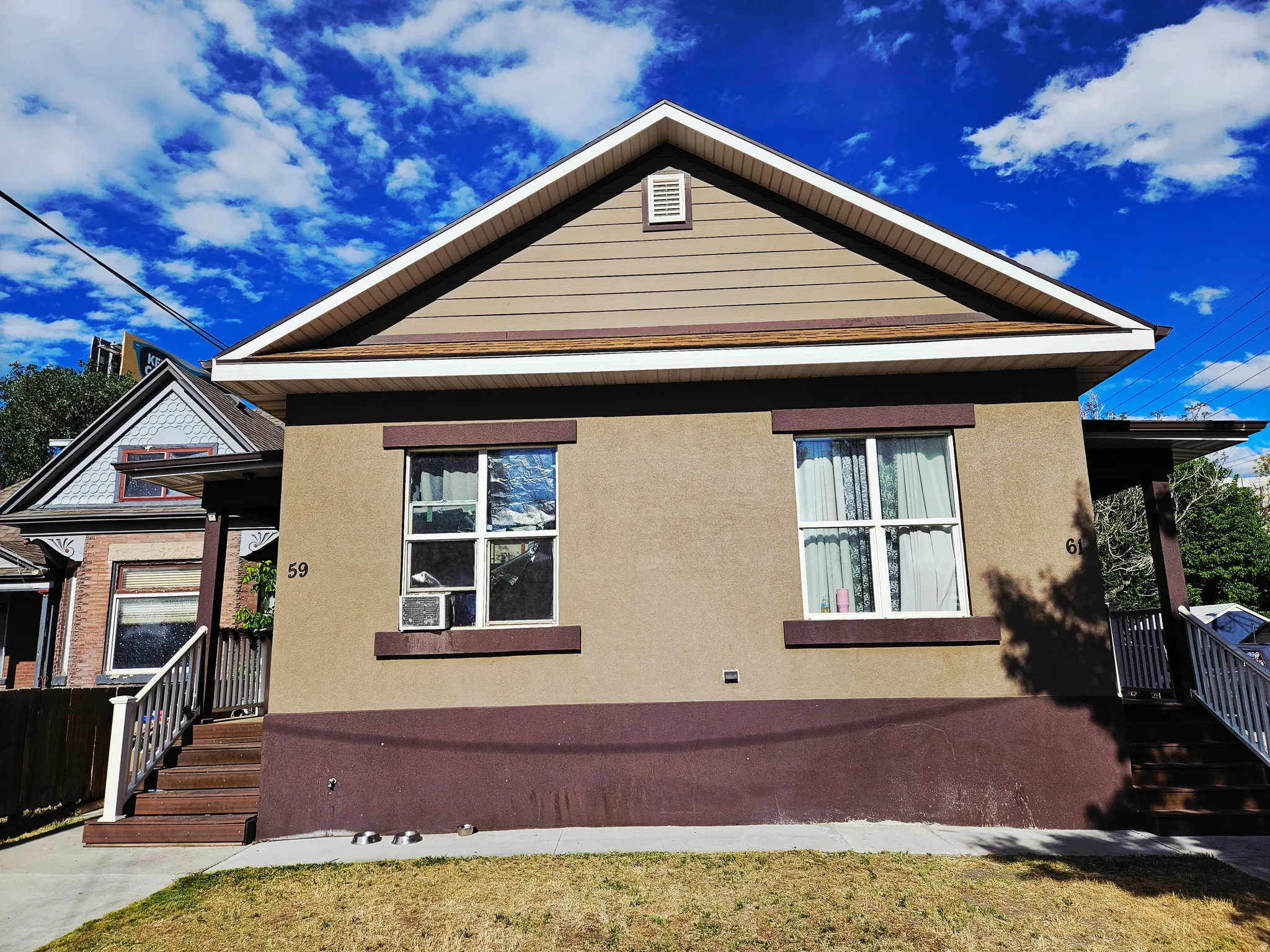 Exterior features include a gabled roofline with brown shingles, tan siding on the gable, and a tan stucco facade with brown trim