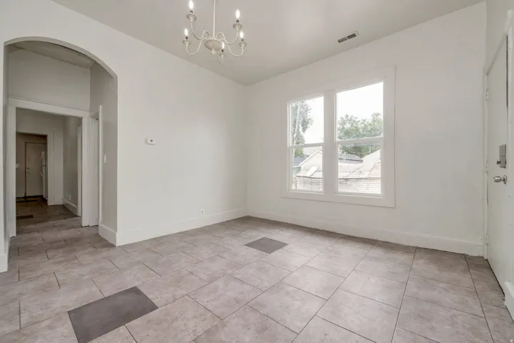 Spacious room featuring neutral tile flooring, white walls, a dual window, and a white chandelier