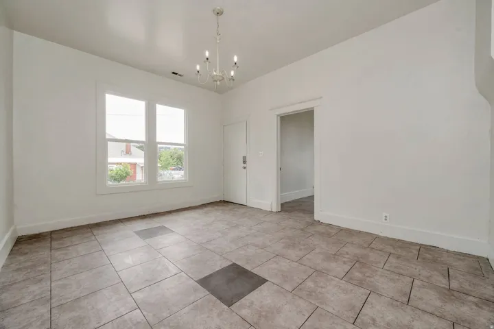 Spacious room featuring neutral-toned tile flooring, white walls, and a multi-pane window
