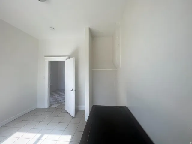 Room featuring light-toned tile flooring, white walls, and a built-in shelf