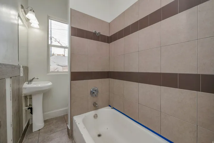 Full bathroom featuring a pedestal sink, a bathtub with a shower fixture, and a tiled shower surround