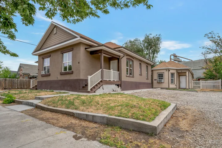 Stucco exterior with contrasting trim details, a covered porch with white railings, and a gravel parking area