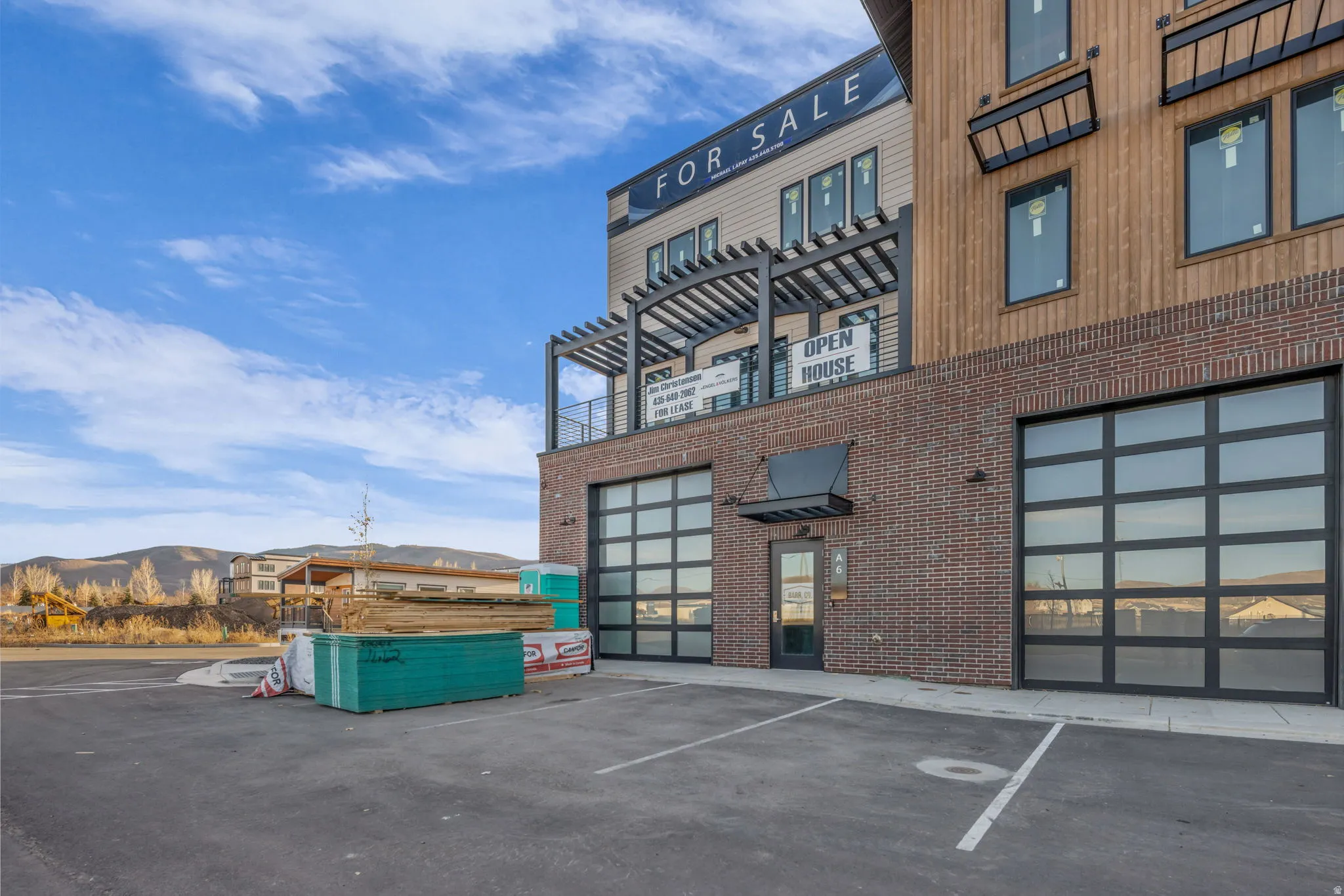 Contemporary multi-level building featuring a brick base, wood-panel siding, and a prominent balcony with a pergola