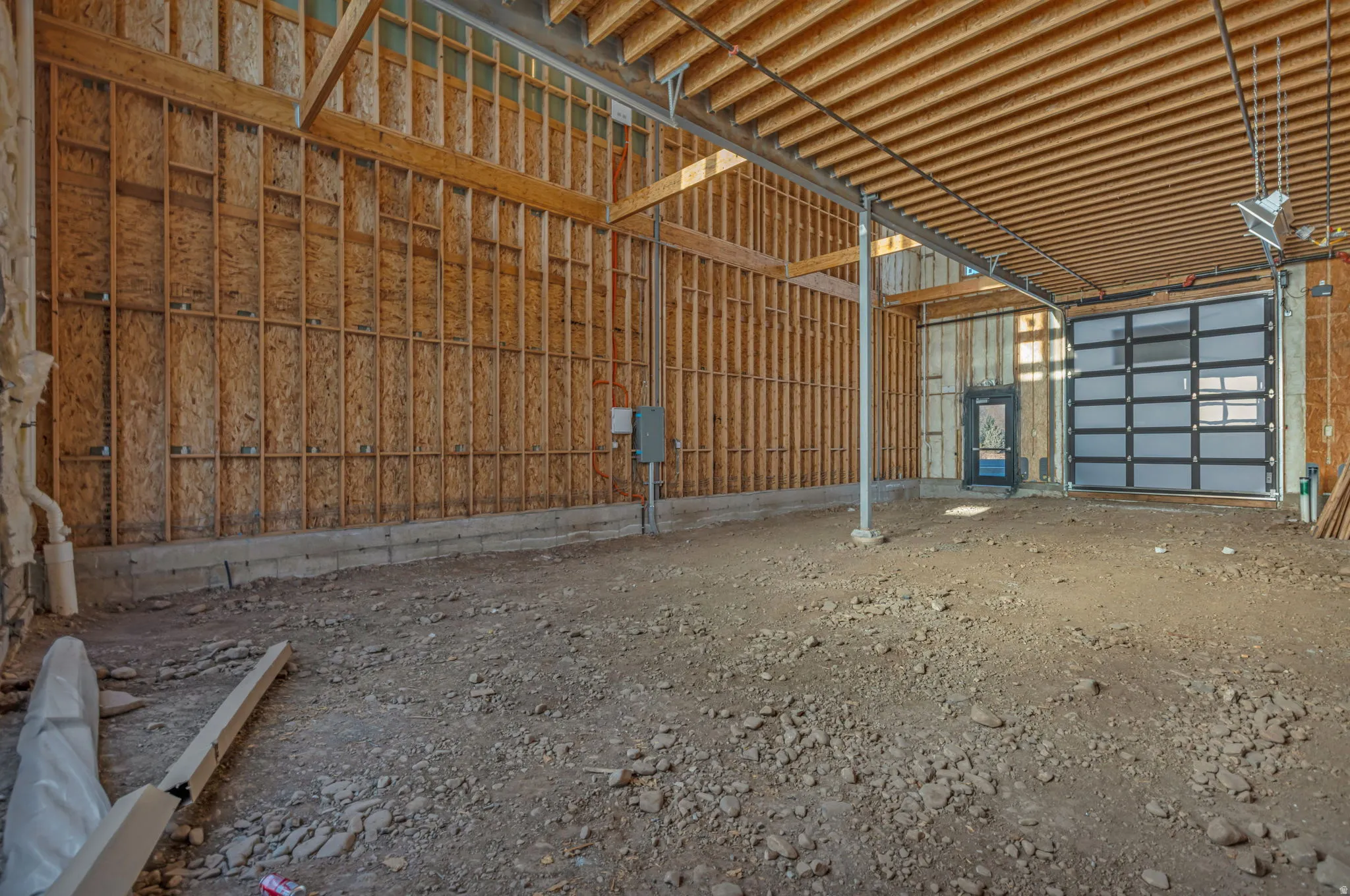 Large unfinished interior space featuring exposed wood framing, an overhead structural beam, and a paneled garage door with frosted window inserts