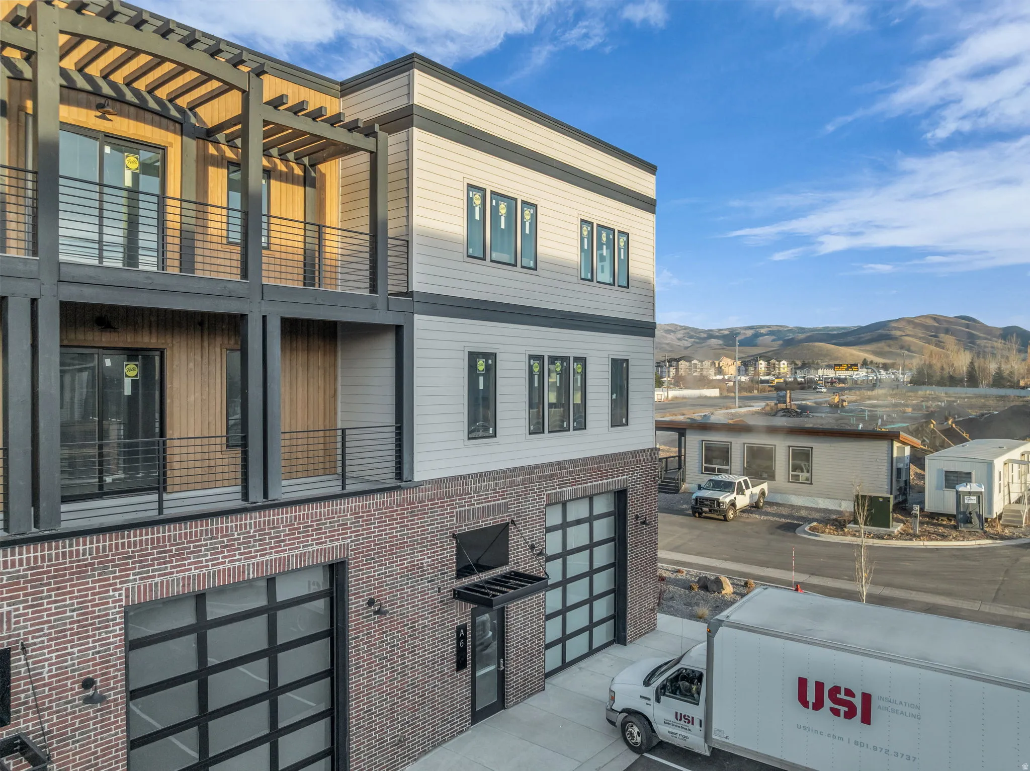 Contemporary multi-level residence featuring brick and horizontal siding exteriors, multiple balconies with metal railings, an upper-level pergola, and a drive-under garage with a glass-paneled door