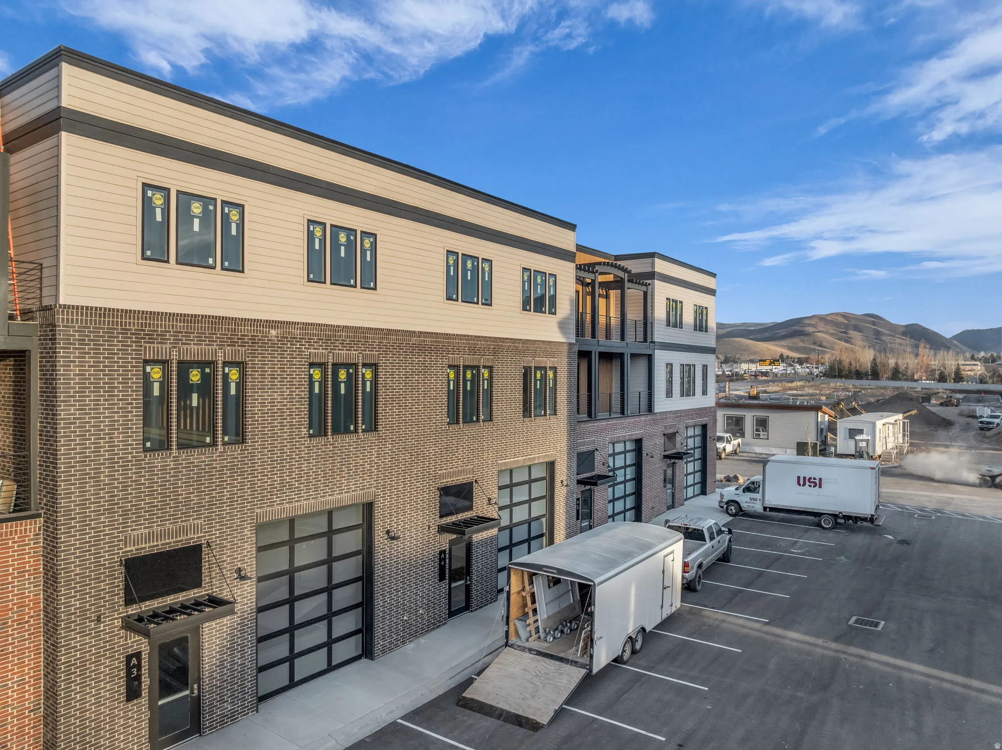 Multi-story building featuring brick and horizontal siding, multiple dark-framed windows, and ground-level glass panel garage doors