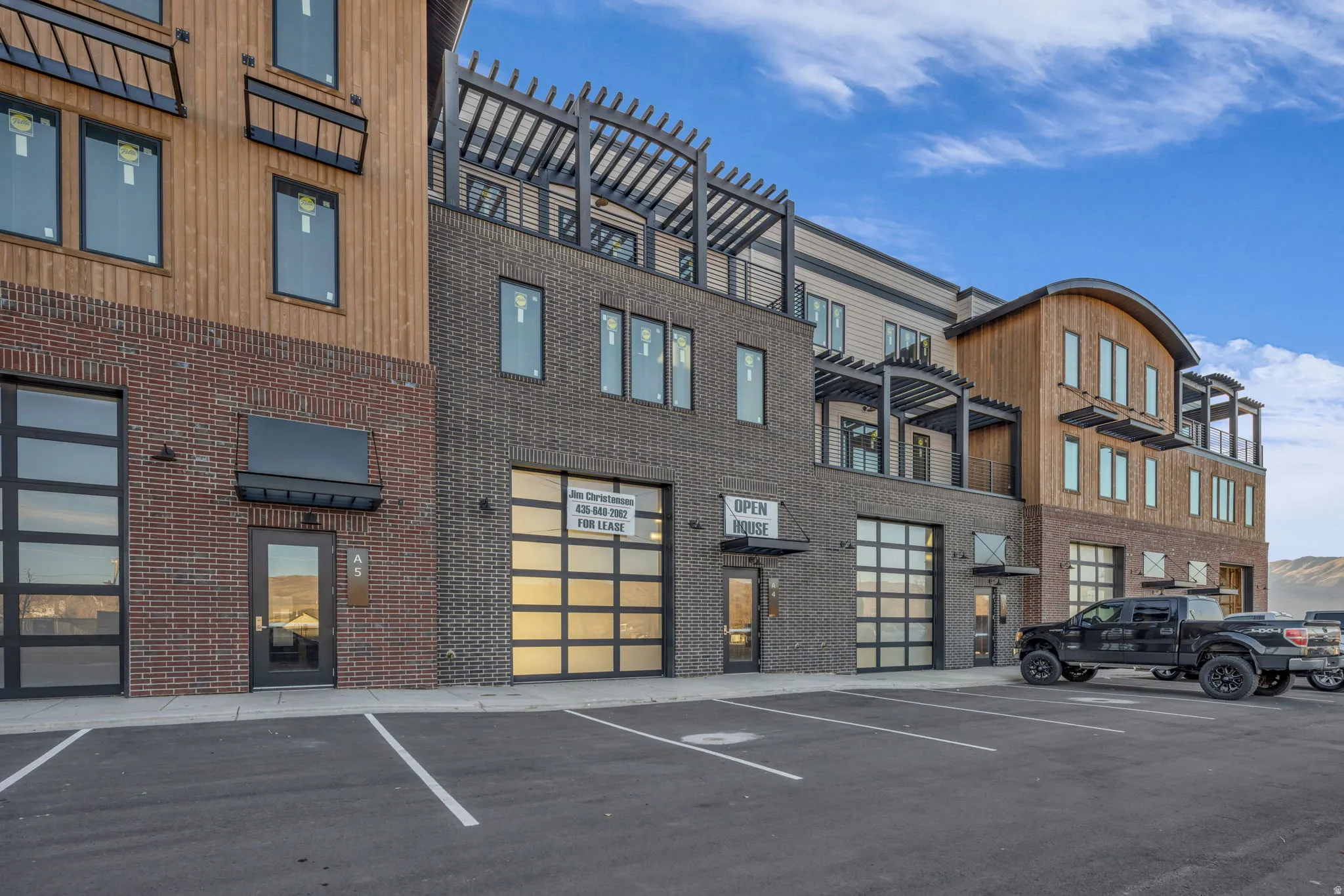 Mixed-material commercial and residential building featuring dark brick, wood-finish siding, and multiple balconies with dark pergolas