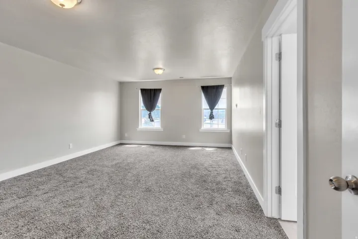 Spacious primary bedroom featuring neutral grey walls and new grey carpeting
