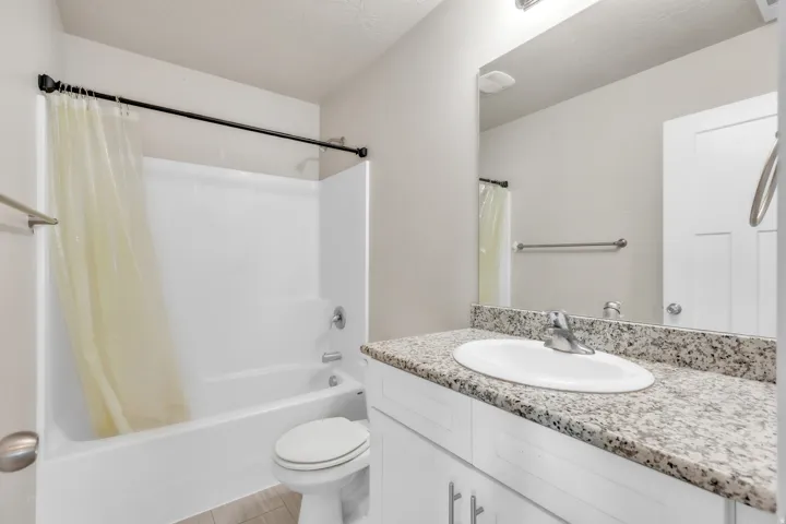 Bathroom featuring an integrated tub-shower unit, white vanity with granite-finish countertop, undermount sink, and tile flooring