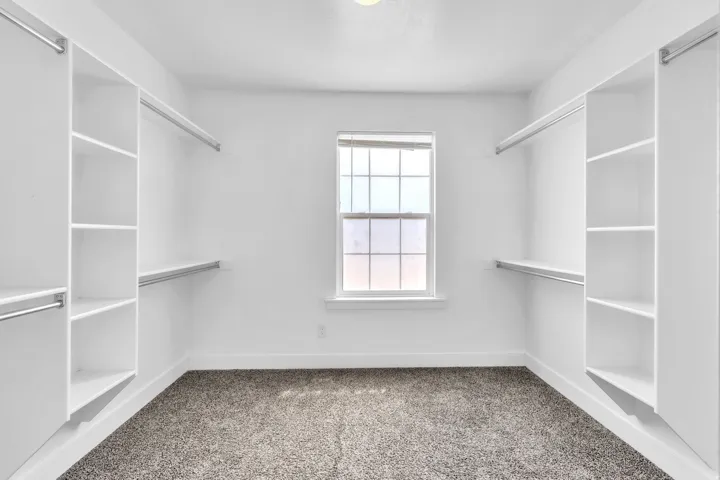 Walk-in closet featuring white built-in shelving, hanging rods, and a central window for natural light