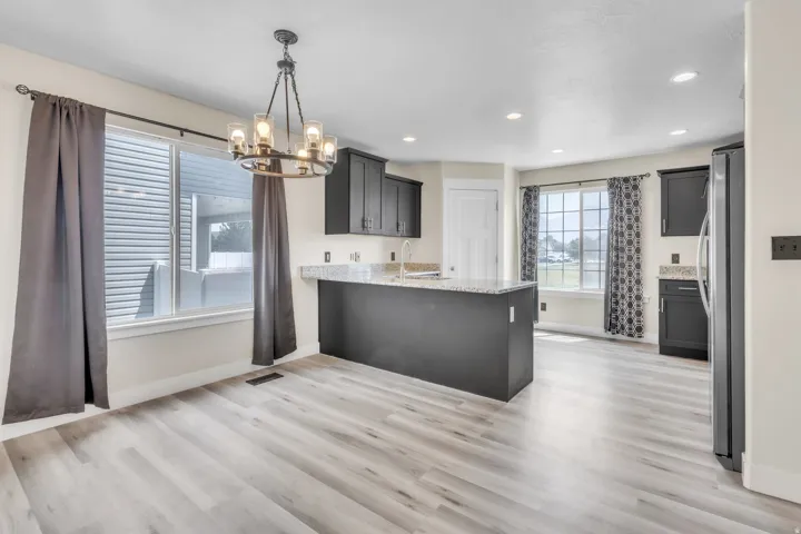 Open-concept kitchen and dining area featuring light wood-finish flooring, dark cabinetry, and granite countertops