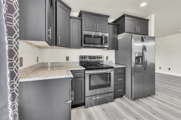 Kitchen featuring dark gray cabinetry, light speckled countertops, stainless steel appliances, and light wood-finish flooring