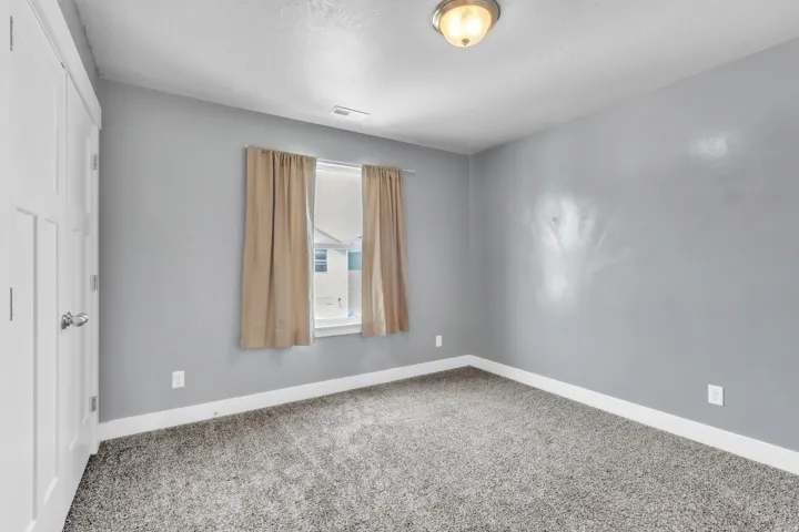Neutral-toned walls featuring textured wall-to-wall carpeting, white baseboards, and a window with natural light