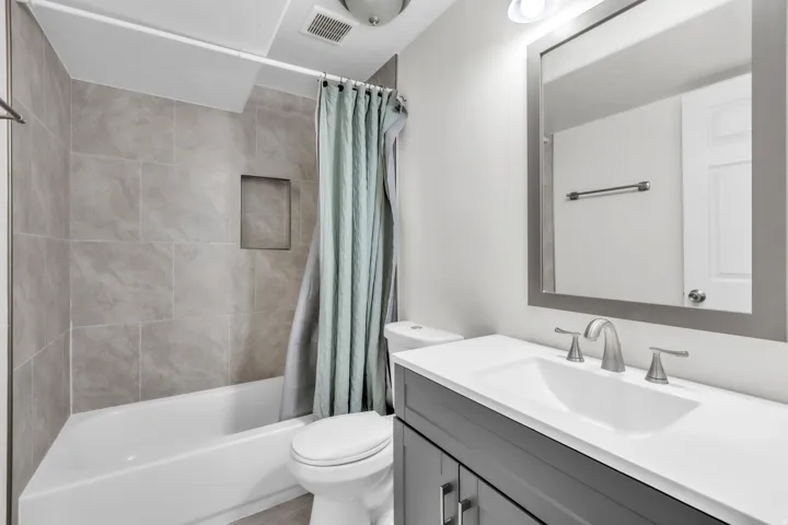 Bathroom featuring a white bathtub, gray large format tile surround with an integrated niche, a white toilet, and a vanity with a white countertop and gray cabinetry