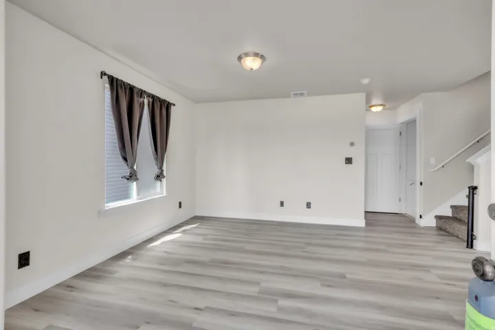 Spacious room featuring light wood-finish flooring, white walls, and a window with blinds