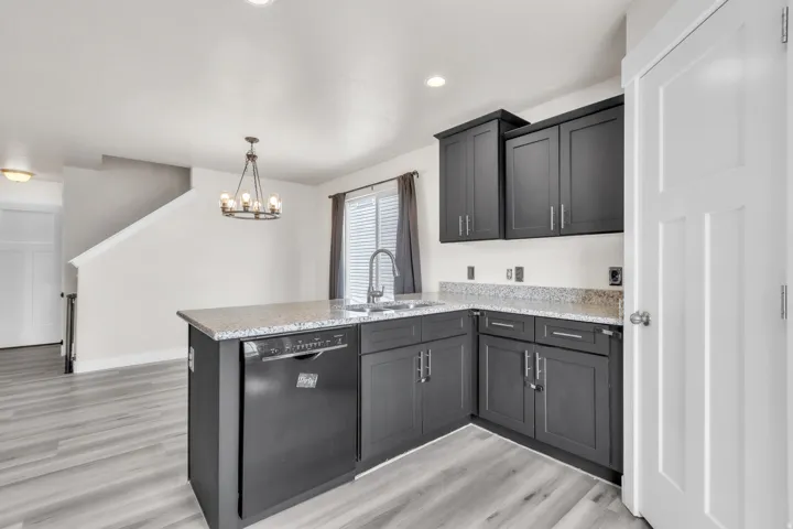 Kitchen featuring dark shaker-style cabinetry, light granite countertops, a stainless steel sink with a high-arc faucet, and an integrated dishwasher