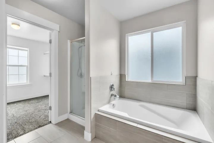 Soaking tub with a tiled surround, chrome fixtures, and a frosted privacy window in the primary bathroom