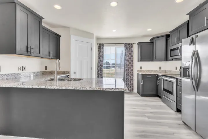 Spacious kitchen featuring dark cabinetry, stainless steel appliances, light granite countertops, recessed lighting, and wood-finish flooring