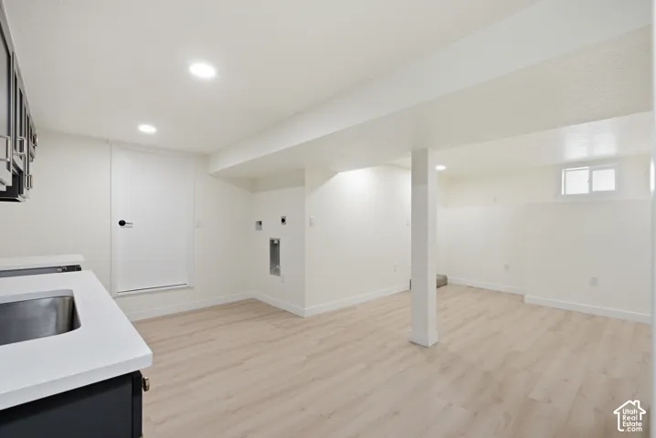 Spacious lower level featuring light wood-finish flooring, recessed lighting, and a utility sink with a solid surface countertop