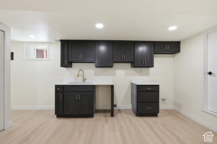 Lower-level space featuring wood-finish flooring, recessed lighting, and a built-in wet bar with dark cabinetry, a white countertop, and a gold-tone faucet