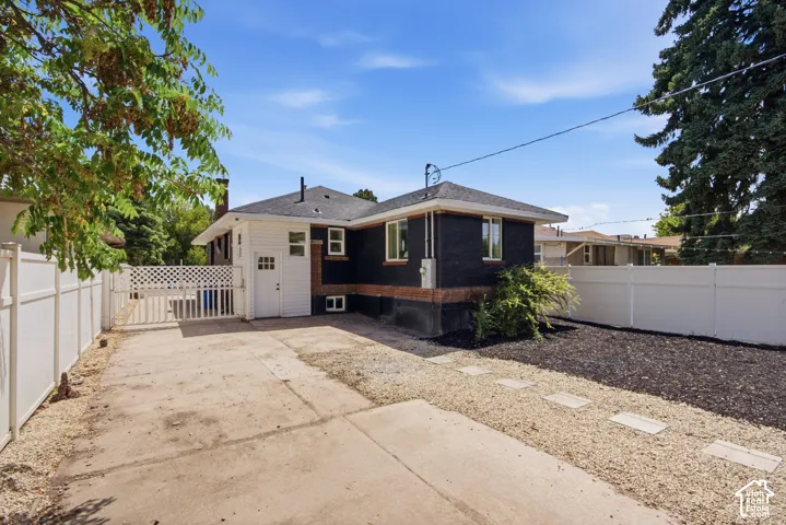 Rear exterior featuring white vinyl fencing, a concrete driveway, and a gravel walkway with stepping stones