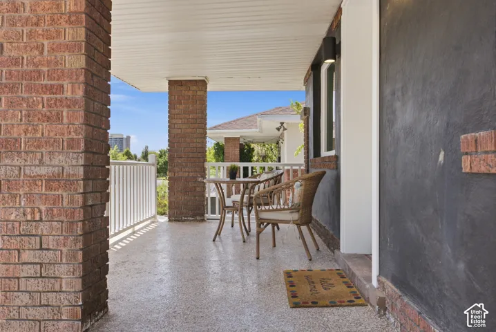 Covered porch featuring brick support columns, white railing, and a textured concrete floor
