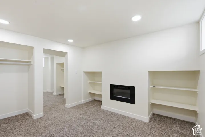 Recessed electric fireplace with built-in shelving, plush carpet flooring, recessed lighting, and a window for natural illumination