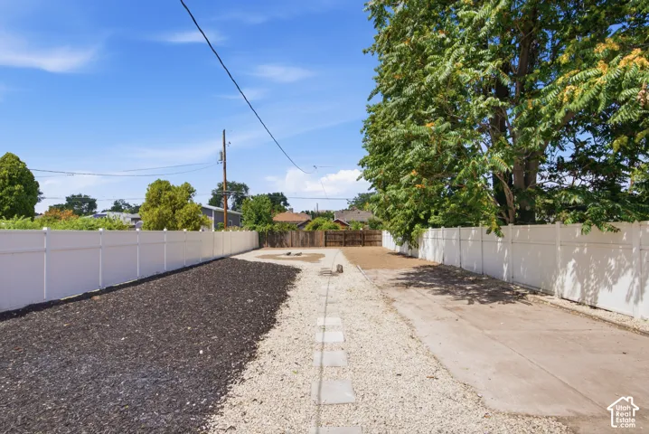 Spacious outdoor area featuring a white privacy fence, gravel and mulch landscaping, and mature trees