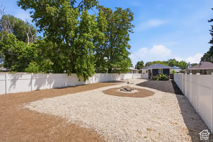 Spacious backyard featuring a white vinyl privacy fence, gravel landscaping, a central fire pit, and a dark-toned exterior residential structure