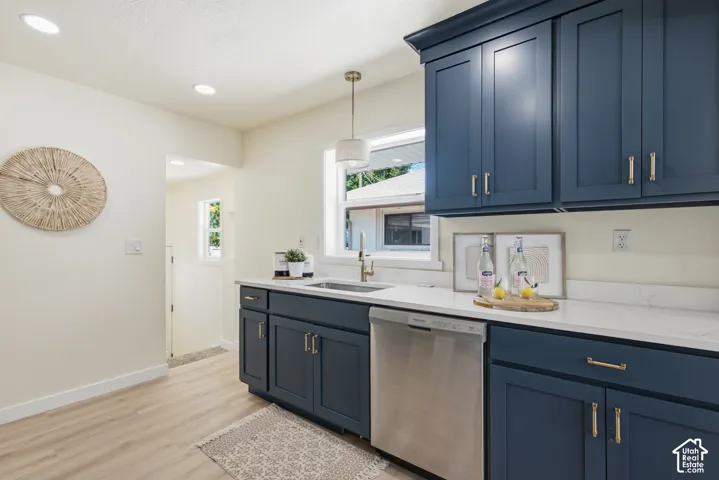 Kitchen featuring blue shaker-style cabinetry with gold-toned hardware, white solid surface countertops, and a stainless steel dishwasher