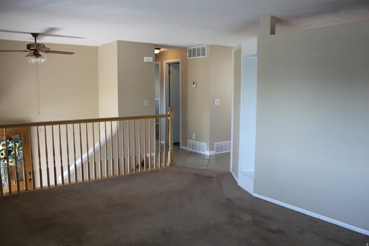 Open concept landing with wood-finish railing, ceiling fan with light fixture, and neutral carpeting