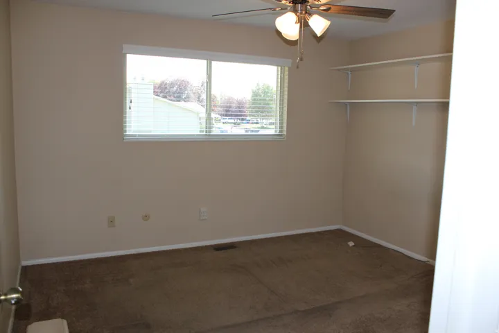 Window with blinds, wall-mounted shelving, and ceiling fan with integrated lighting
