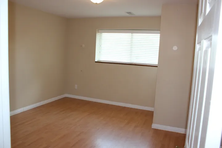Wood-finish flooring with white trim, a single window with blinds, and a flush-mount ceiling light