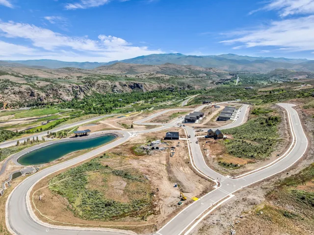 Aerial perspective showcasing a developing community with paved roads, a central water feature, and mountain scenery