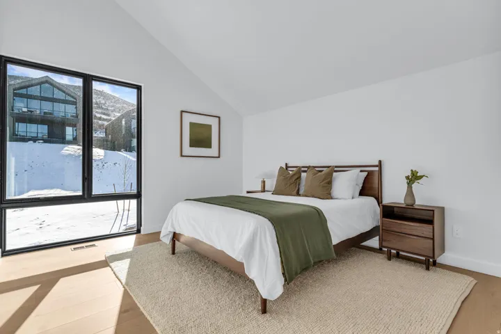 Expansive window feature with black framing, wood-finish flooring, vaulted ceiling, and white wall finishes