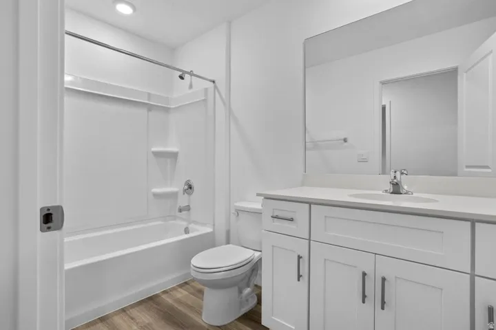 Full bathroom featuring a white tub and shower combination with an integrated storage niche, a single-sink vanity with white cabinetry, a light-toned countertop, and wood-finish flooring