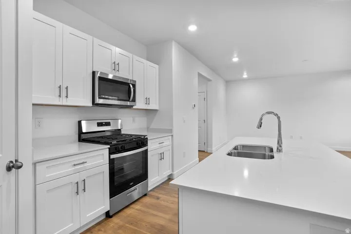 Modern kitchen featuring white shaker cabinetry, stainless steel appliances, white countertops, and wood-finish flooring