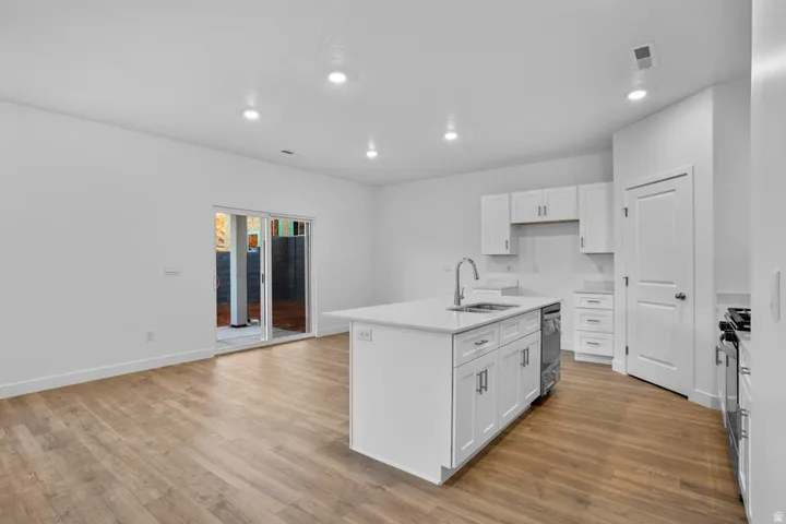 Open-concept kitchen featuring an island with an integrated sink and gooseneck faucet, white cabinetry, and wood-finish flooring throughout