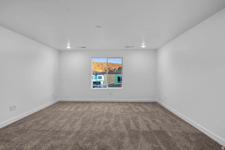 Spacious room featuring neutral carpeting, white walls, and a window framing distant mountains