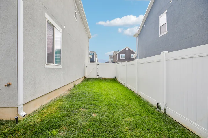 Side yard with a grass lawn, white vinyl fencing, and a white vinyl gate