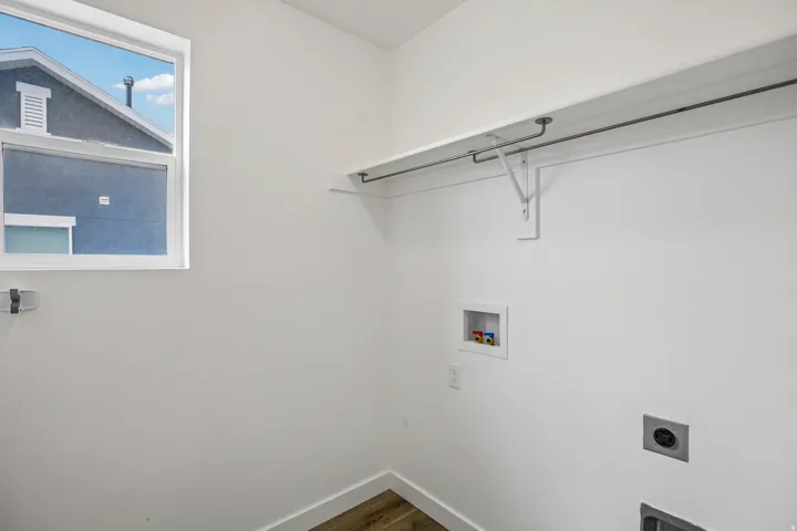 Utility room with a window, white walls, wood-finish flooring, and a built-in shelving unit with a hanging rod