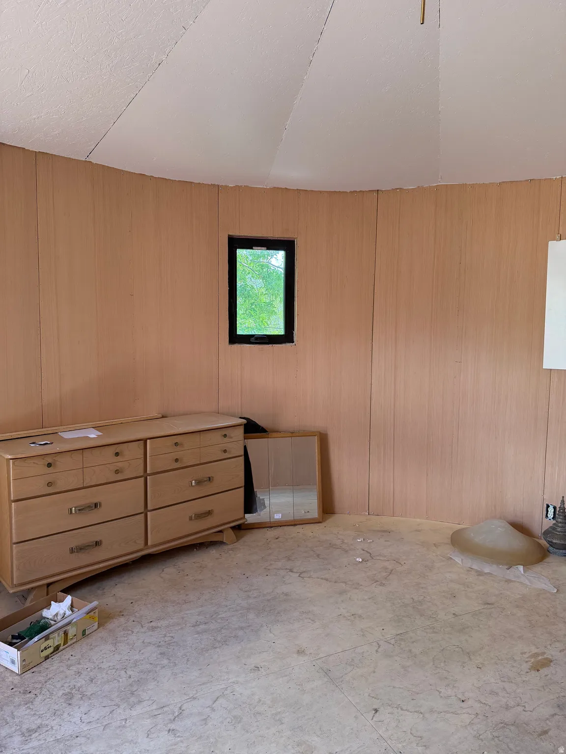 Curved interior wall paneling with a single window, textured ceiling, and unfinished flooring