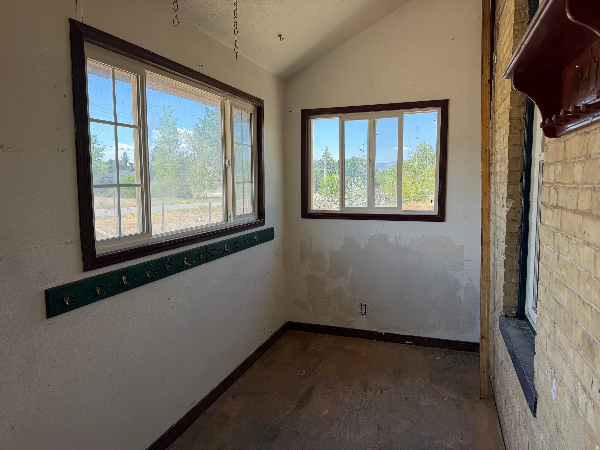 Enclosed porch featuring multiple windows, sloped ceiling, wood-finish baseboards, and a brick exterior wall