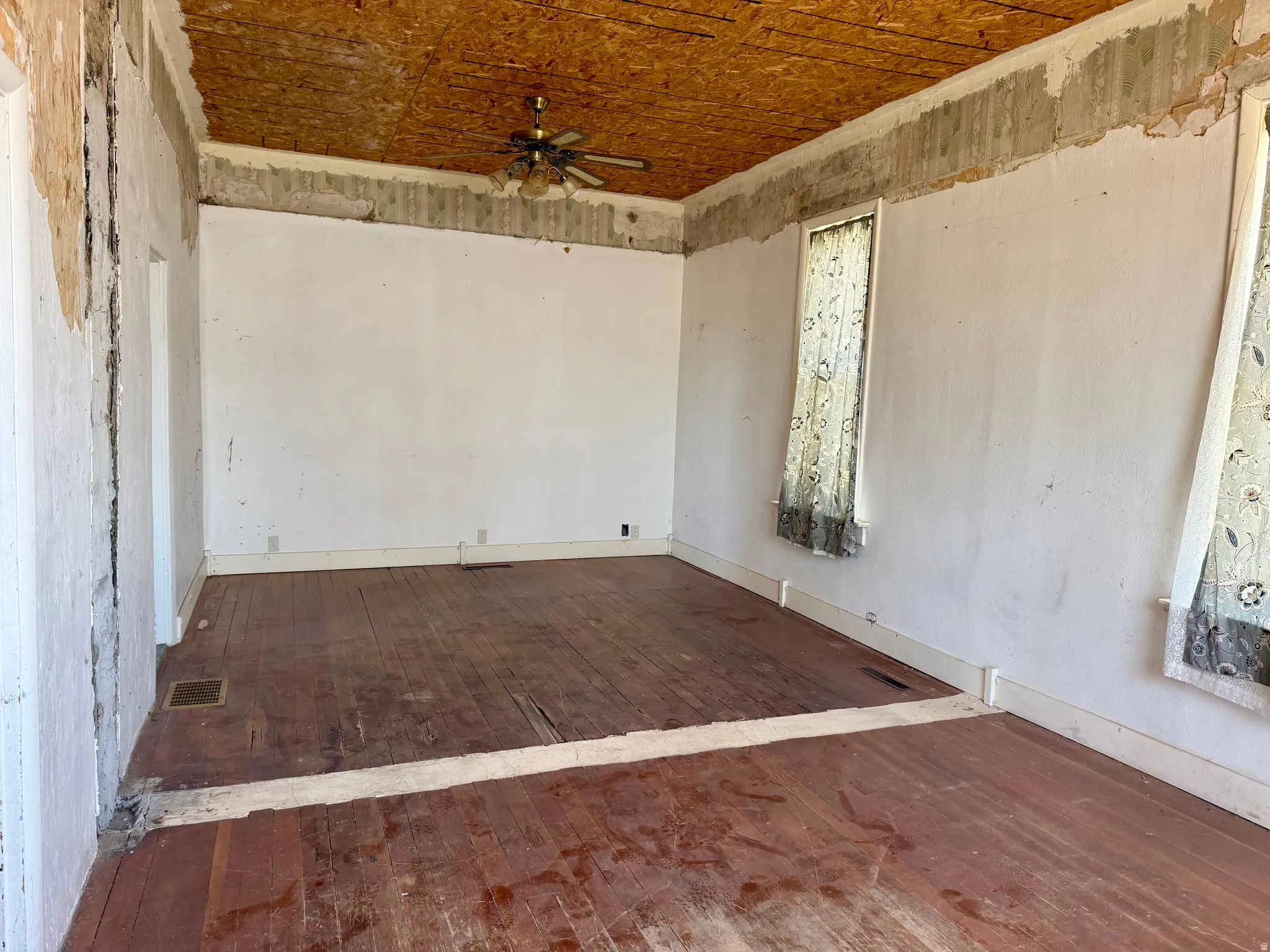Spacious interior room featuring wood-finish flooring, white baseboards, and a ceiling fan with integrated lighting